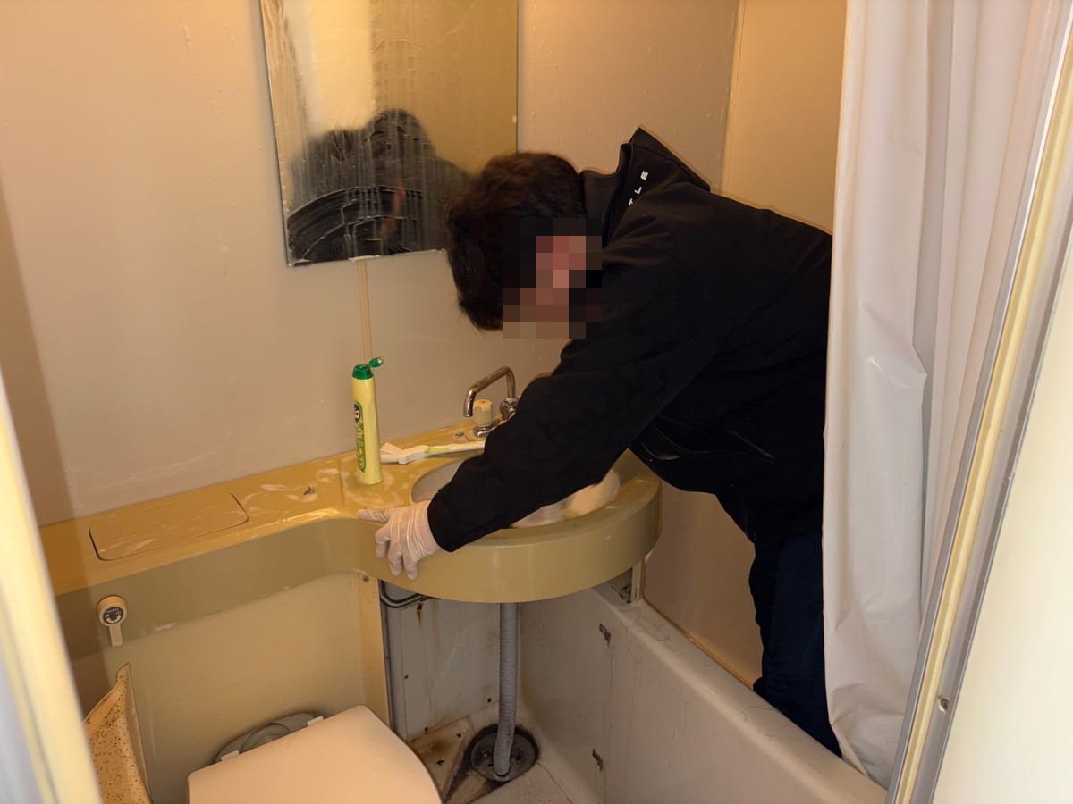 浴室の洗面台を手袋と道具を使って清掃している様子