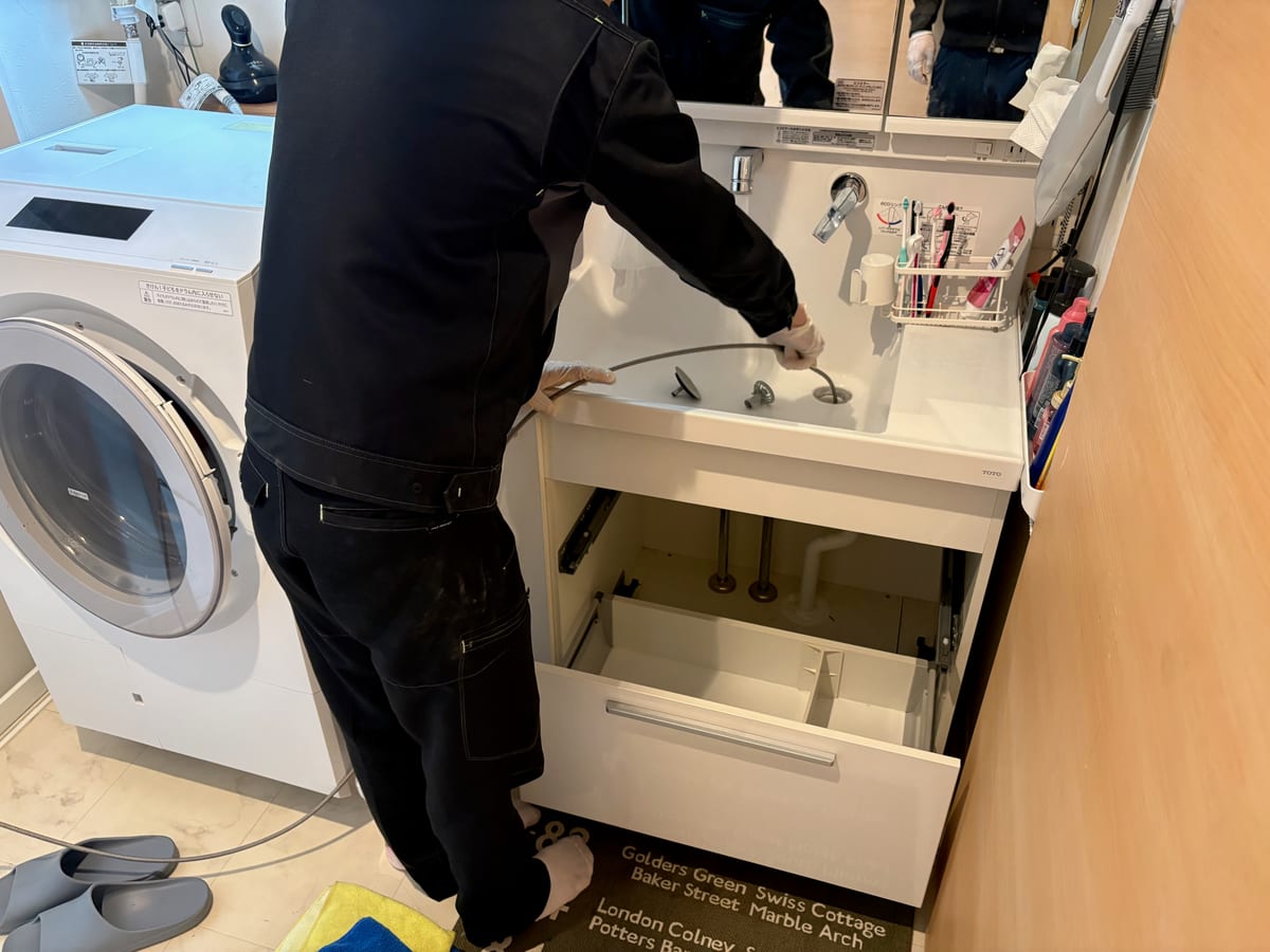 洗面台の排水まわりを道具で清掃する手元