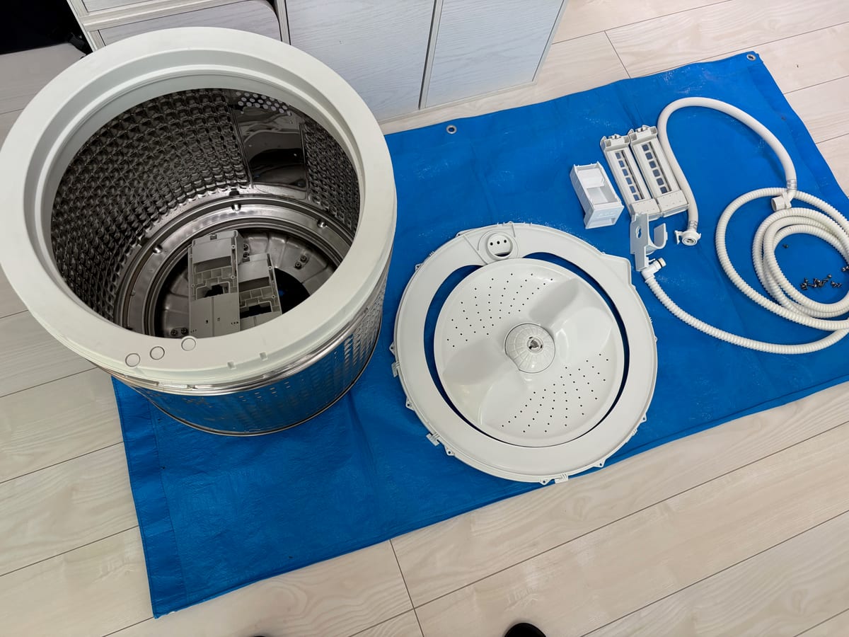 養生シートの上に整然と並べたドラム式洗濯機の槽と分解部品